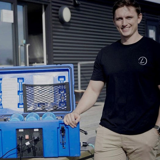 Two men standing with a blue toolbox and equipment outside a building.